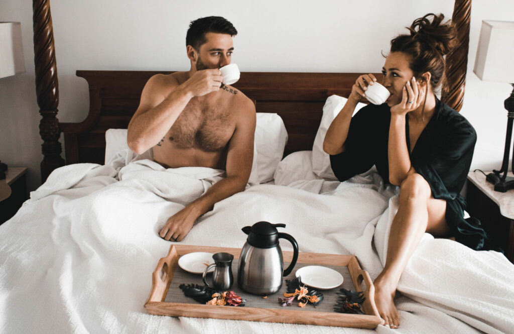 Couple enjoying their honeymoon phase, sitting in bed drinking coffee